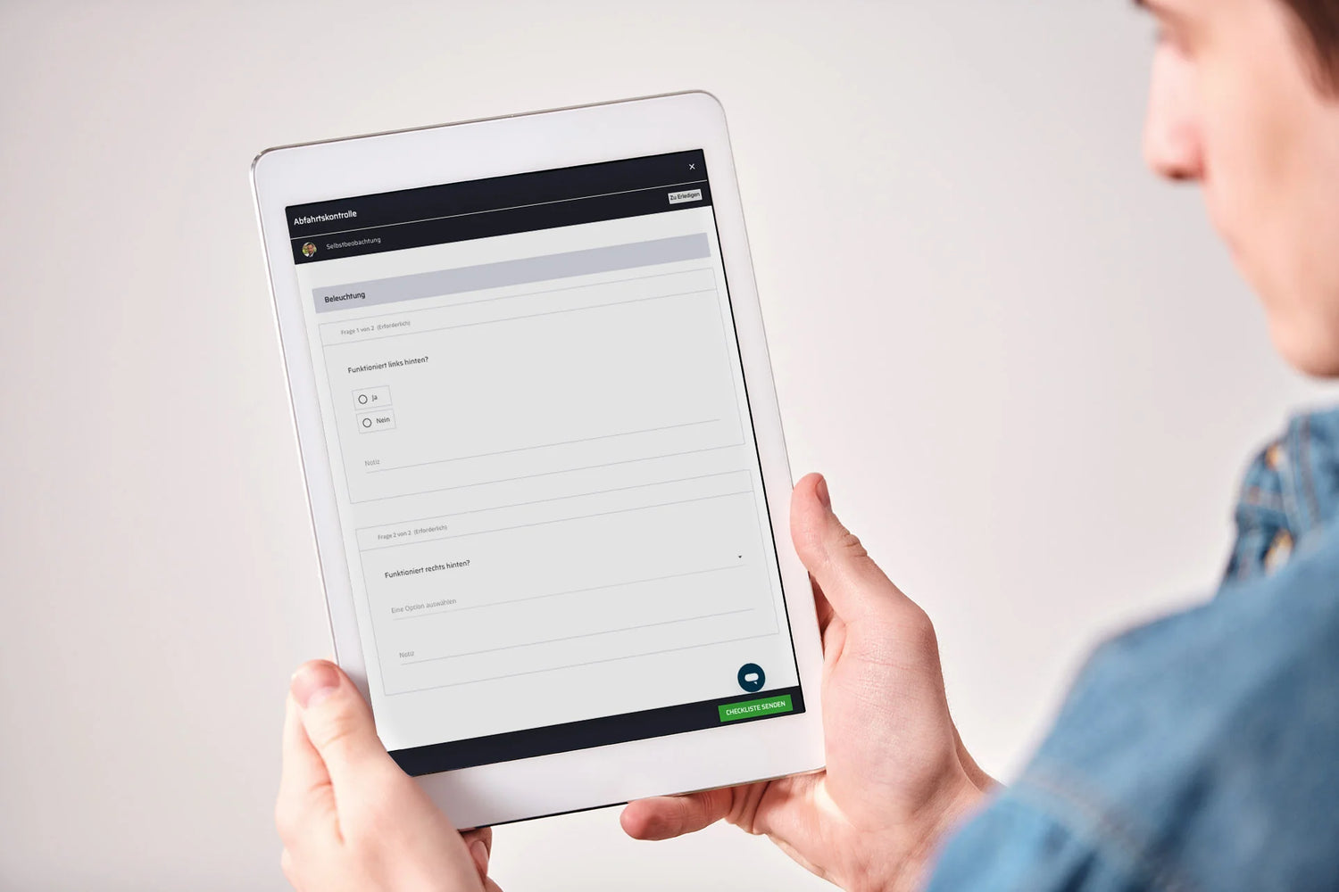 Mann mit Jeanshemd hält ein Tablet mit einer digitalen Beobachtungscheckliste in den Händen.