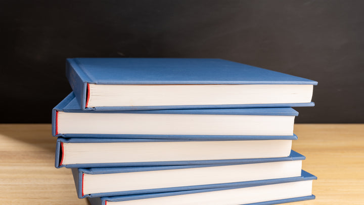Bücherstapel auf Holztisch und schwarze Tafel im Hintergrund. 